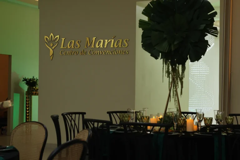 Mesa esmeralda con centro de palma y el logo de Las Marías al fondo